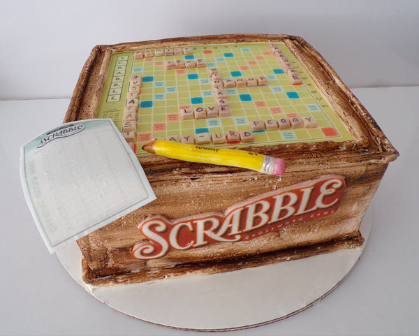 Scrabble-themed cake with tiles and a pencil on a white background