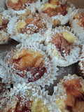 Close-up of several small peach fruit tarts or pastries in white paper cups, topped with powdered sugar and glossy fruit glaze.