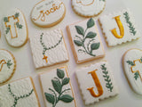 A flat-lay view of decorated sugar cookies with white icing, featuring gold and green floral and cross designs on a light background.