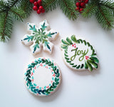 Decorative cookies with green wreaths and 'Joy' text on a wooden surface