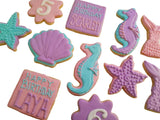 A collection of decorated sugar cookies shaped like seahorses, starfish, a shell, a mermaid tail, and birthday message squares on a light cream background.
